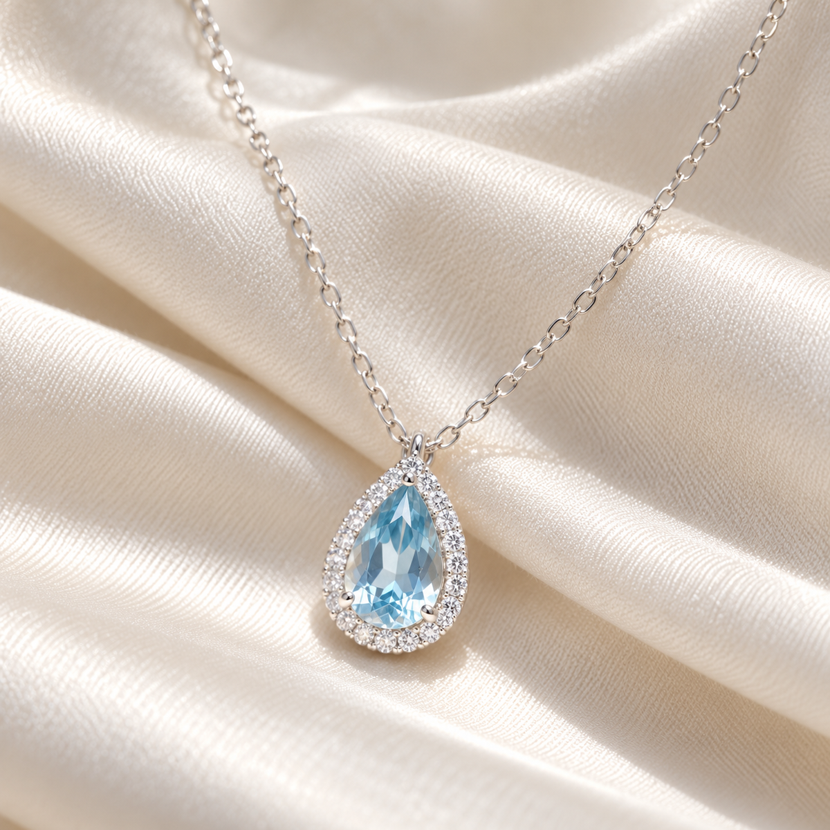 Azure Teardrop Necklace on ivory silk — close-up of blue centre and clear-stone halo